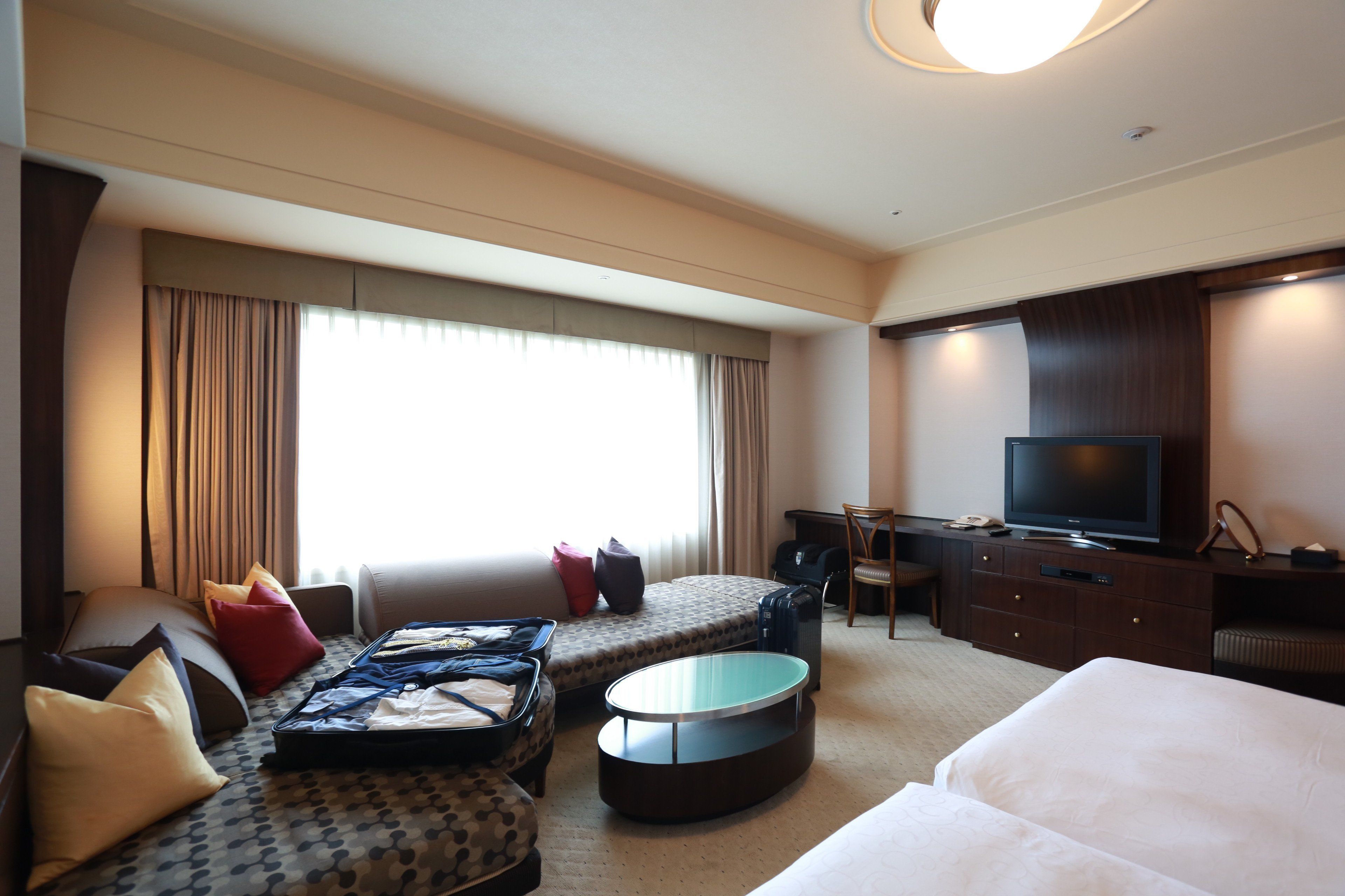 Ein Hotelzimmer mit einem großen Bett, einer Schlafcouch, einem Schreibtisch mit Fernseher und einem Fenster mit Vorhängen.