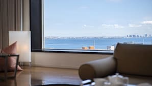 Habitación de hotel con un amplio ventanal que ofrece vistas al horizonte urbano y al mar.