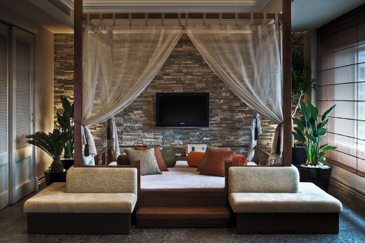 A bedroom with a stone wall, a TV mounted above a bed, and a canopy.