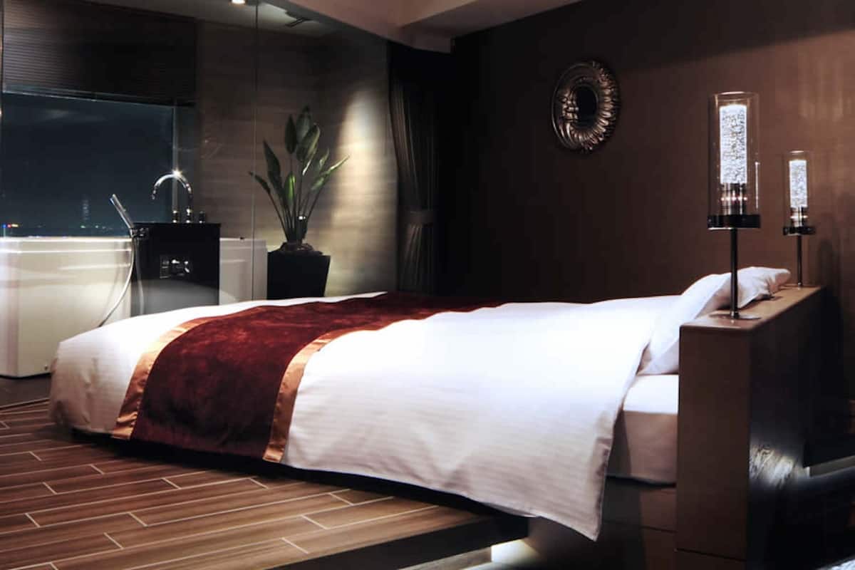 A modern hotel room with a large bed, a potted plant, a small desk, and a view of the city through the window.