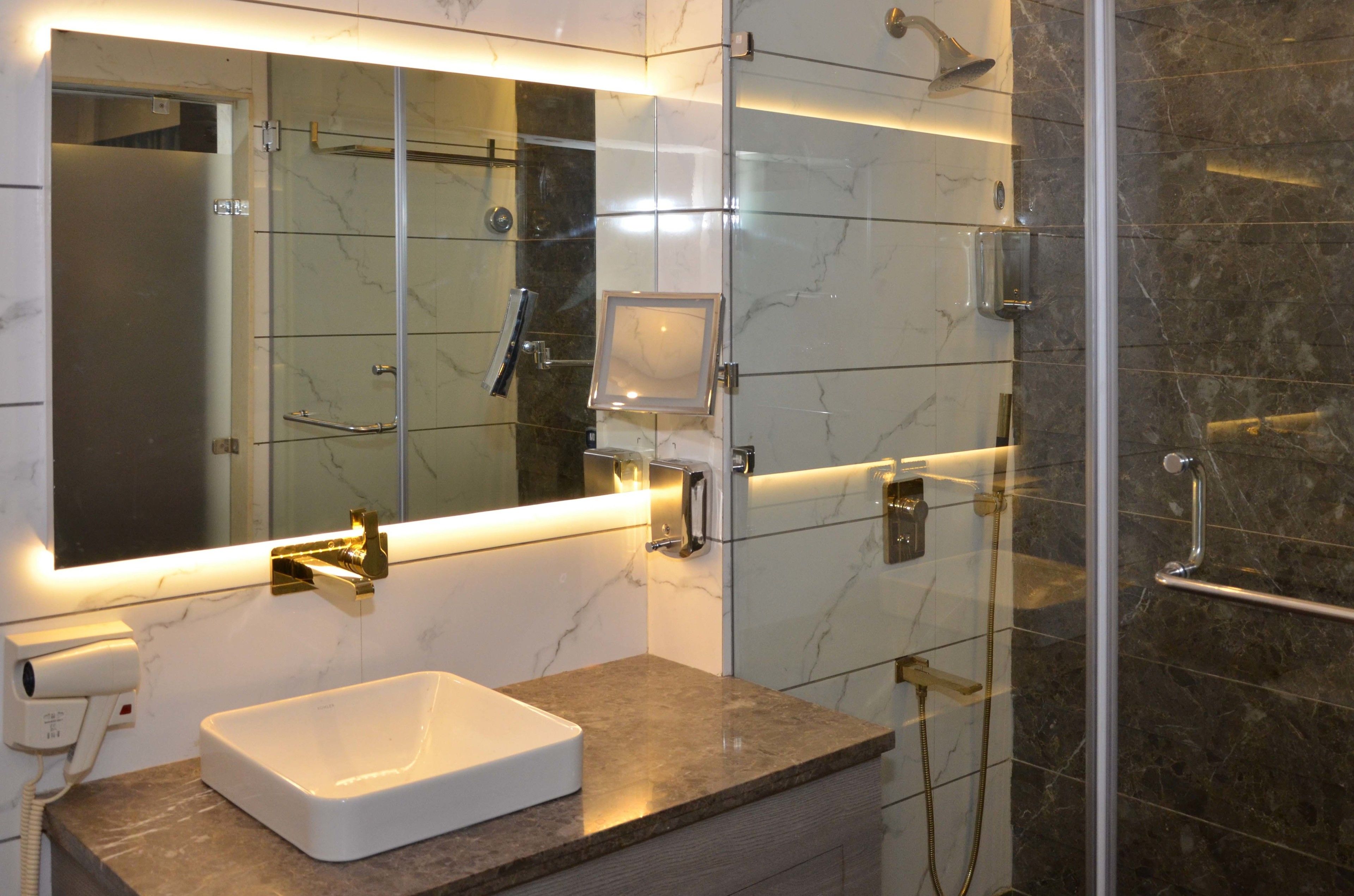 Un bagno moderno con uno specchio grande, un lavandino bianco e una cabina doccia in vetro.