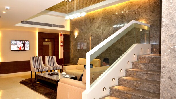 A lobby with a marble staircase, a TV mounted on the wall, and seating areas with striped and plain cushions. - Sawera Grand (Amritsar)