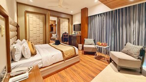 A modern hotel room with a large bed, a desk with a laptop, a chair, a small table with fruit, and a TV. - Sawera Grand (Amritsar)