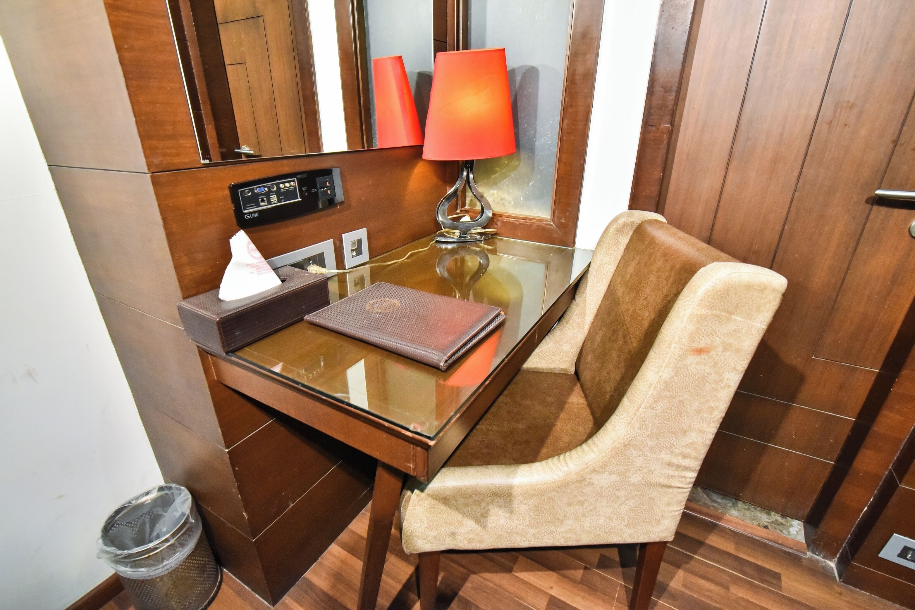 Habitación de hotel con una mesa de vidrio, una silla, una lámpara, una caja de pañuelos y un control remoto.