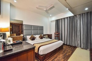 A hotel room with a large bed, a desk with a lamp, a ceiling fan, and a window with curtains.