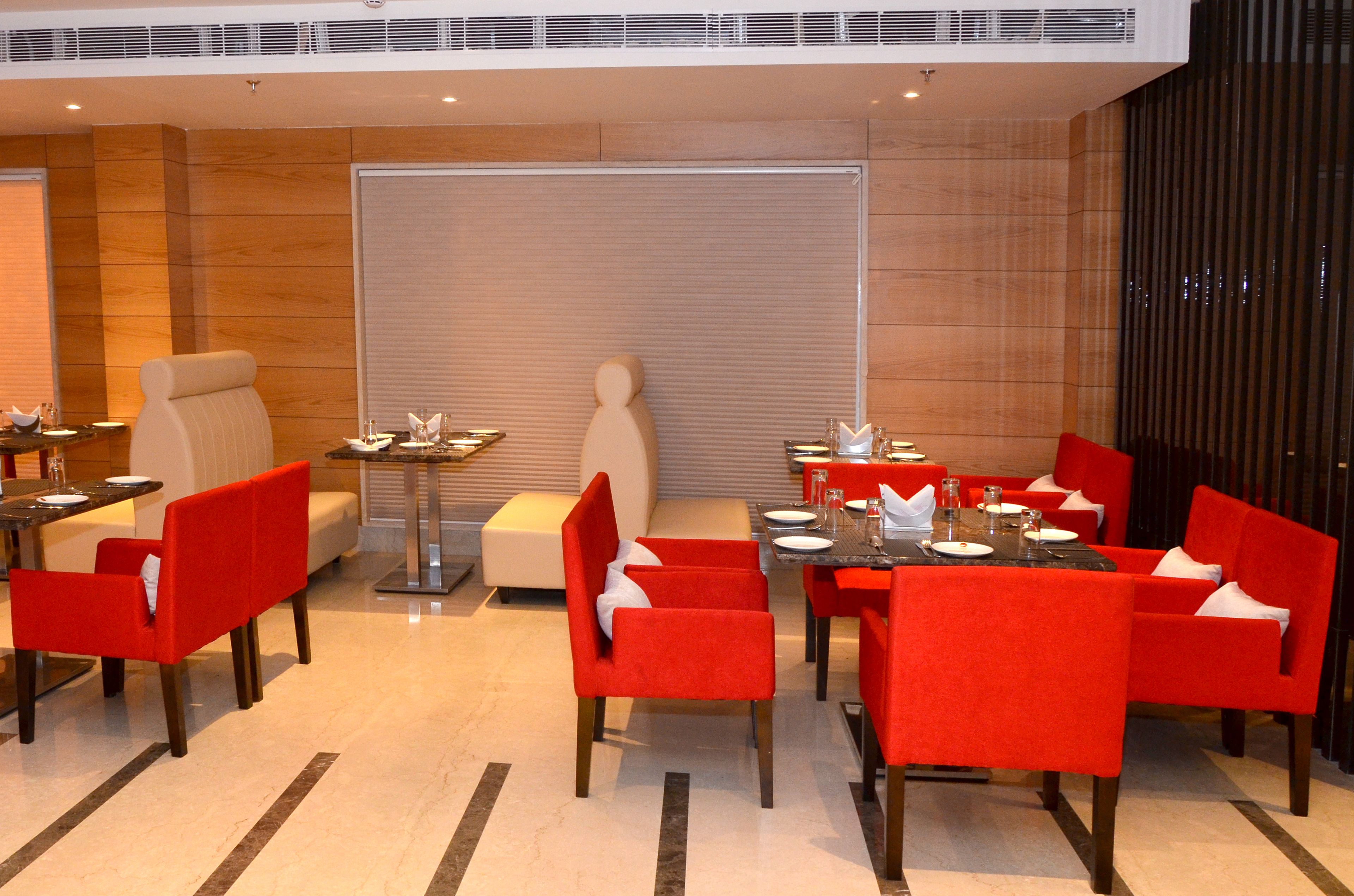 Un espace repas moderne avec des chaises et des tables à revêtement rouge, un canapé blanc et une grande fenêtre équipée de stores.