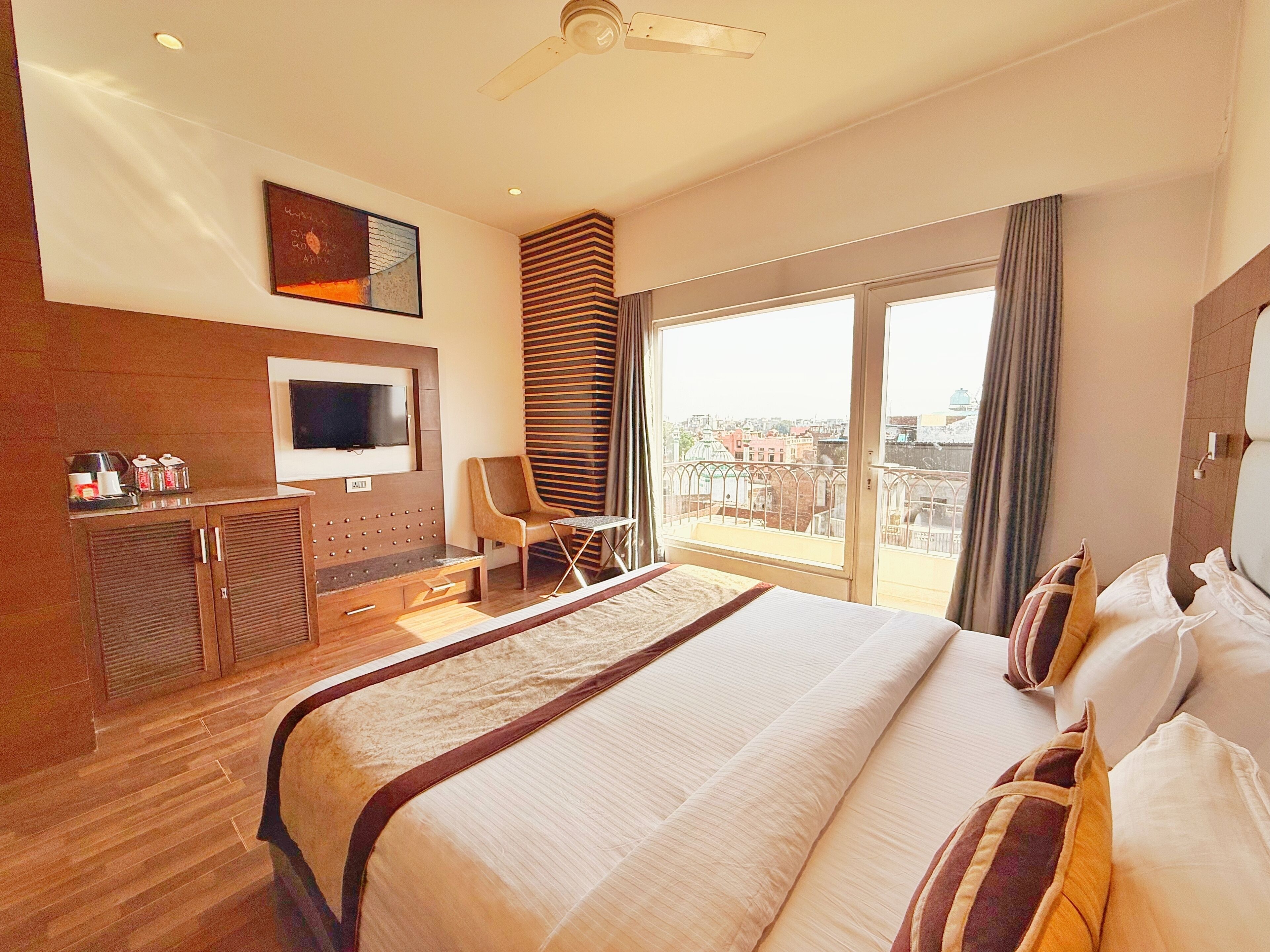 Habitación de hotel con una cama grande, televisión, escritorio con silla, balcón con vistas y ventilador de techo.