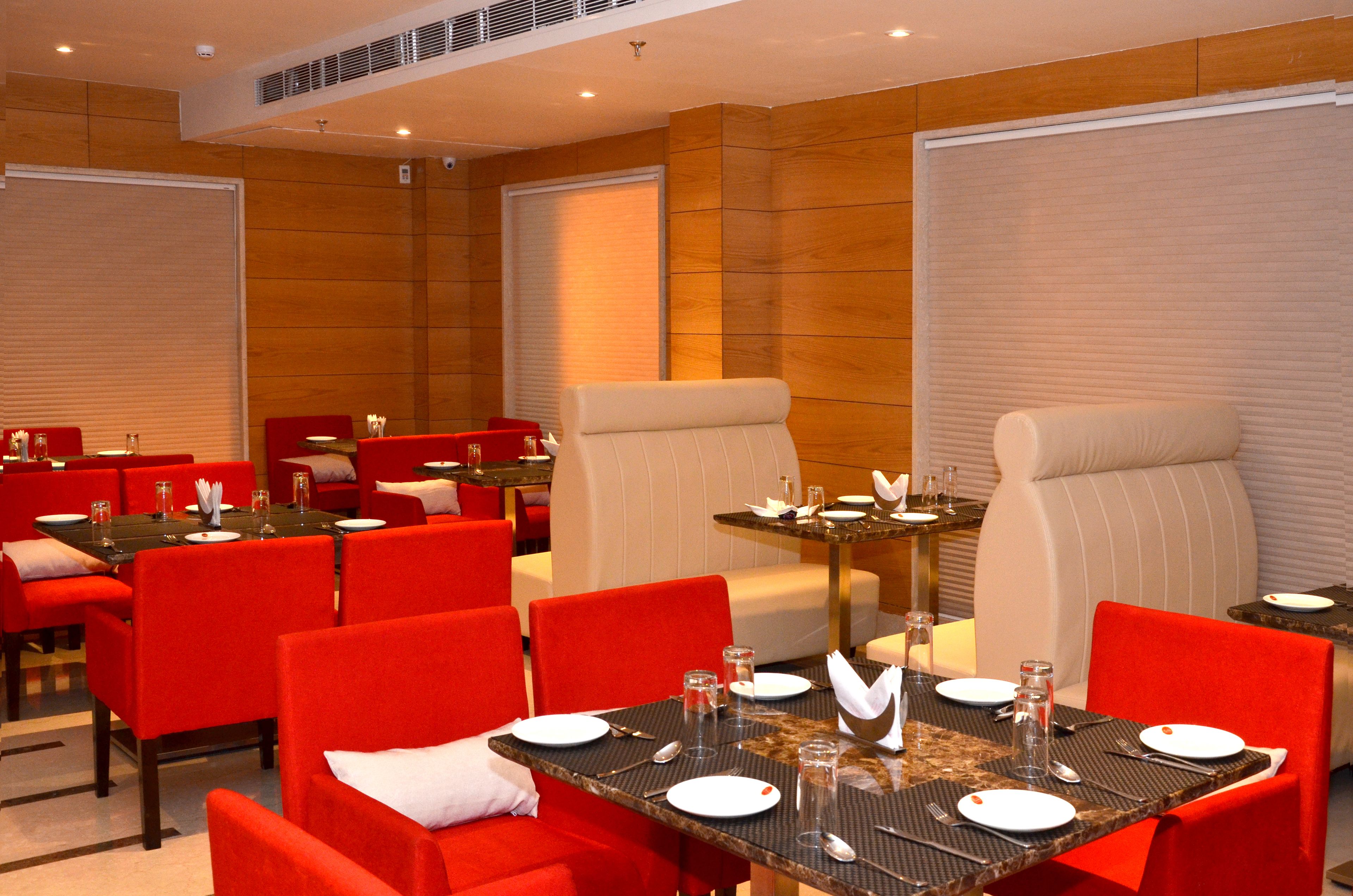 A hotel dining area with red and beige chairs, tables set with plates, glasses, and cutlery.