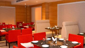 A hotel dining area with red and beige chairs, tables set with plates, glasses, and cutlery.