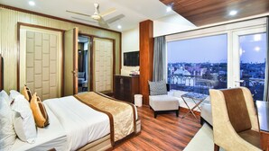 A hotel room with a bed, a chair, a TV, and a balcony with a city view. - Sawera Grand (Amritsar)