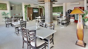 A spacious dining area with multiple tables and chairs, a decorative pillar, and a television screen.