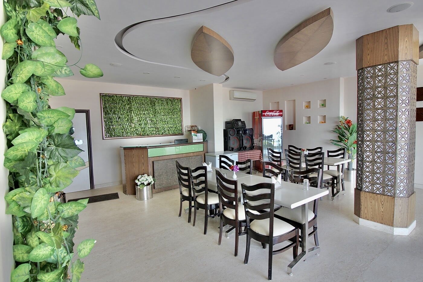 A modern dining area with a central table, surrounded by chairs, and a decorative plant on the left.