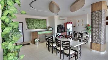 A modern dining area with a central table, surrounded by chairs, and a decorative plant on the left.