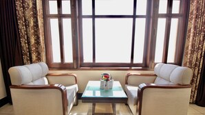 A room with two beige armchairs, a small table with a vase of flowers, and a window with curtains.