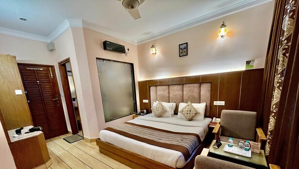 A hotel room with a large bed, a desk with a chair, a wardrobe, and a mirror.