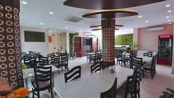 A restaurant with multiple tables and chairs, a decorative pillar, and a Coca-Cola refrigerator.