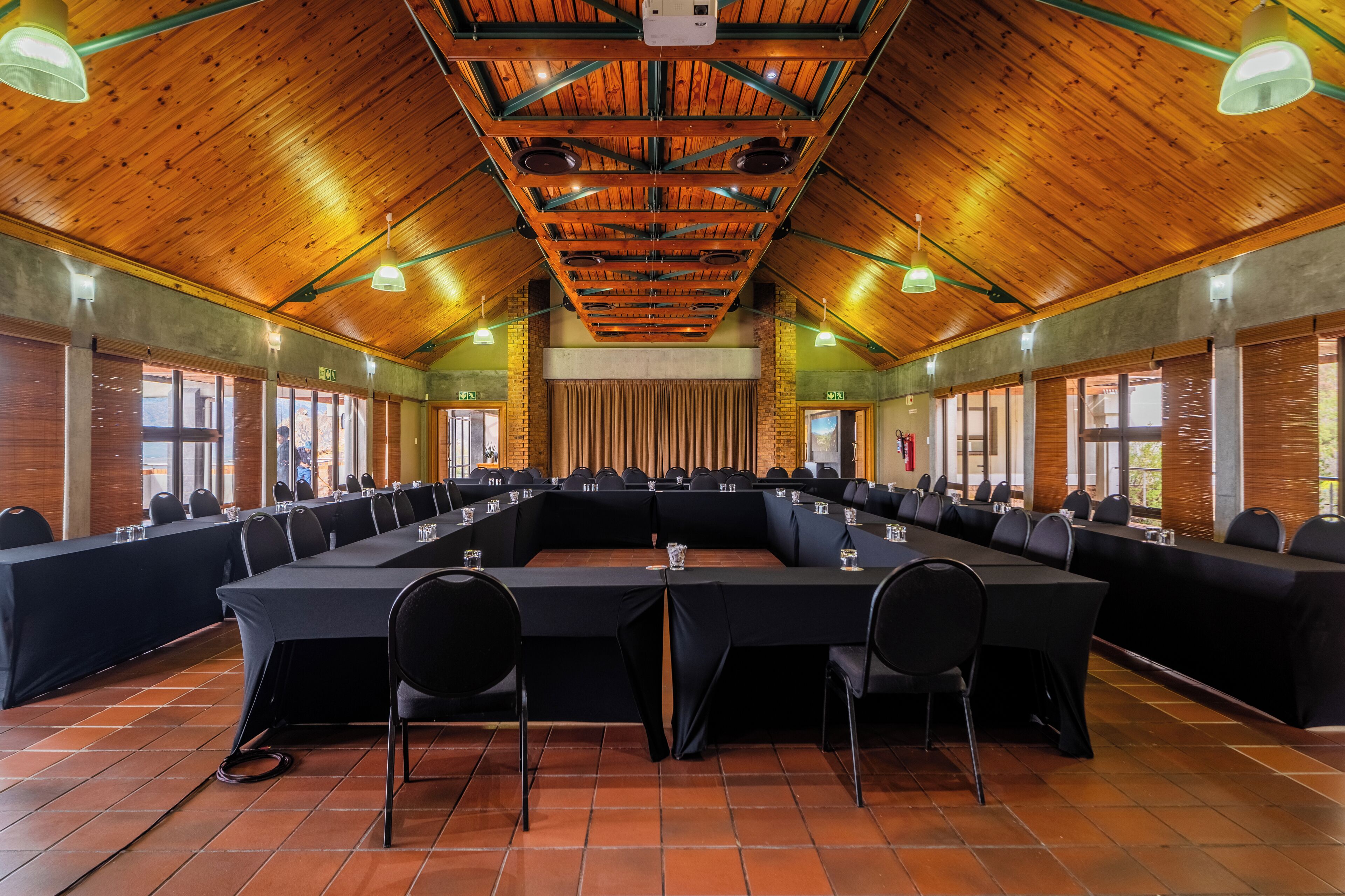 Una sala conferenze con un lungo tavolo, sedie nere e travi in legno al soffitto.