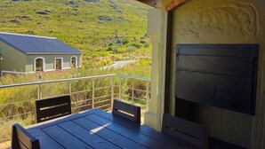 A covered patio with a table and chairs, a brick oven, and a view of a house and mountains. - ATKV Goudini Spa (Rawsonville)