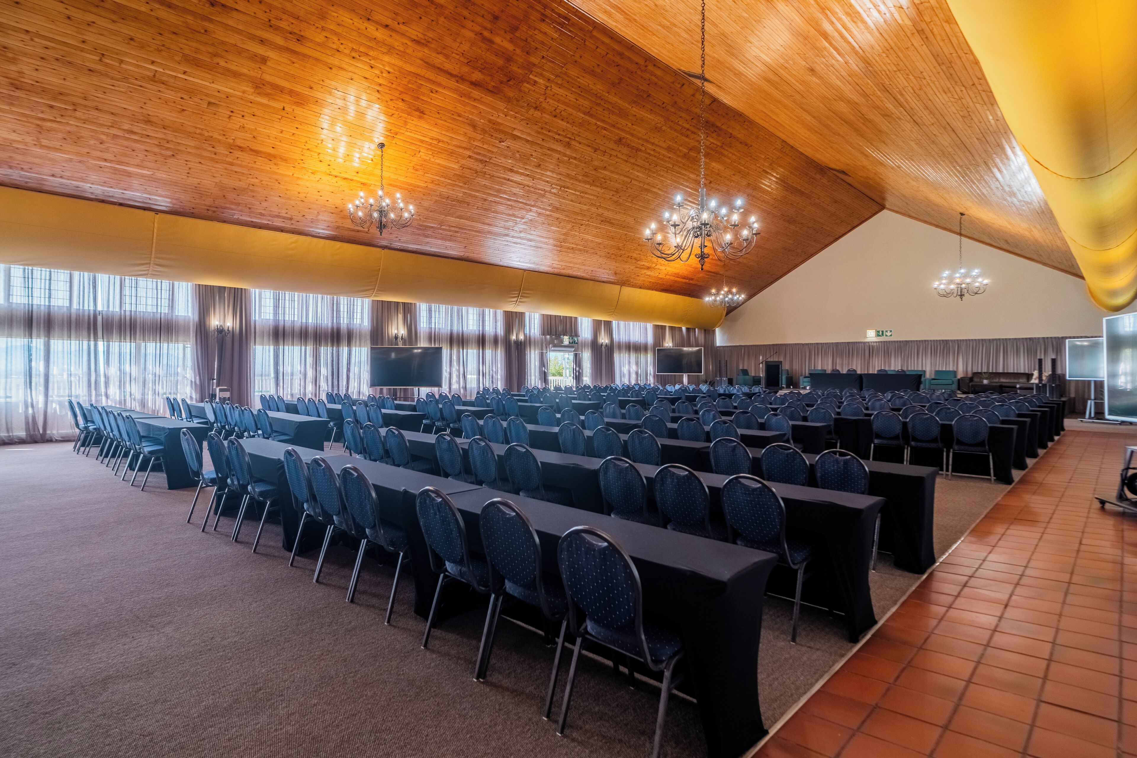 A large conference room with rows of tables and chairs, wooden ceiling, and large windows.