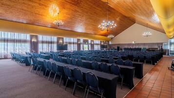 A large conference room with rows of tables and chairs, wooden ceiling, and large windows.