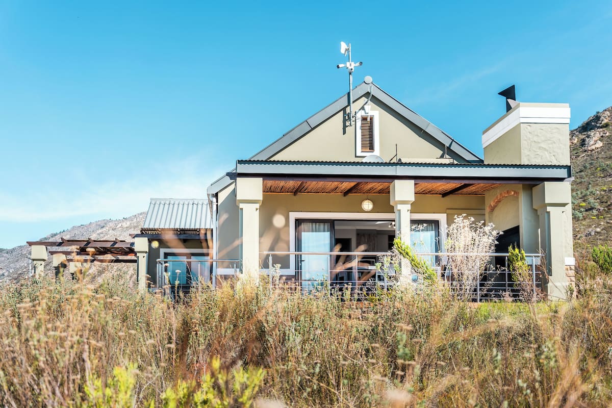 A modern house with a covered porch, a satellite dish, and a mountain backdrop.