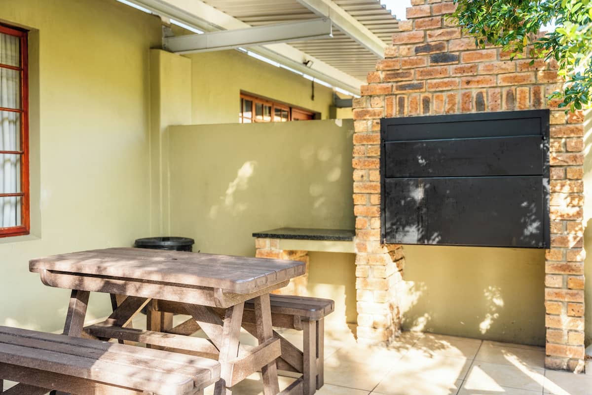 A patio area with a wooden table and benches, a brick wall, and a black grill.