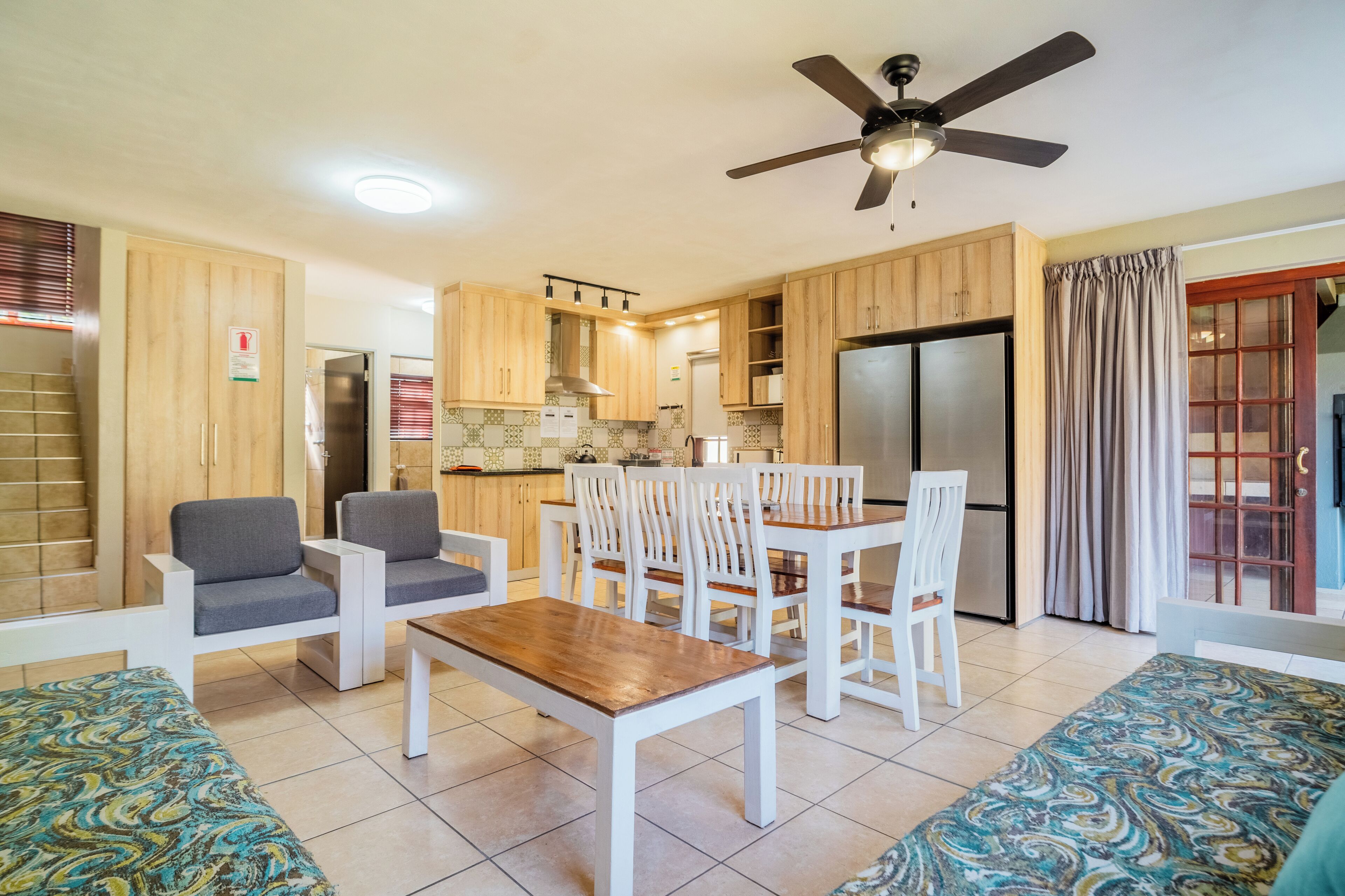 A modern kitchen with wooden cabinets, a dining table with chairs, a ceiling fan, and a refrigerator.
