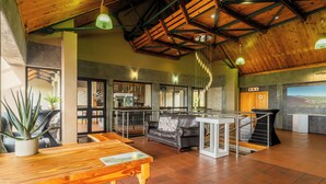 A spacious interior with a high ceiling, wooden beams, a black leather sofa, a wooden table, and a view of the outdoors through large windows. - ATKV Goudini Spa (Rawsonville)
