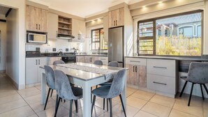 A modern kitchen with a dining area, featuring a large island, built-in appliances, and a view of the outdoors. - ATKV Goudini Spa (Rawsonville)