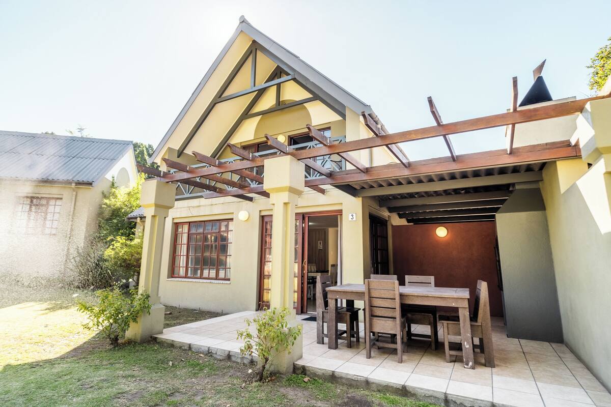A two-story house with a covered patio area, a dining table, and chairs.