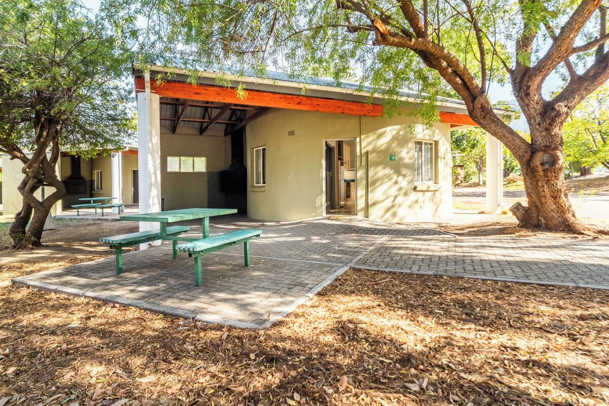 A covered outdoor seating area with picnic tables and a building with a red roof.