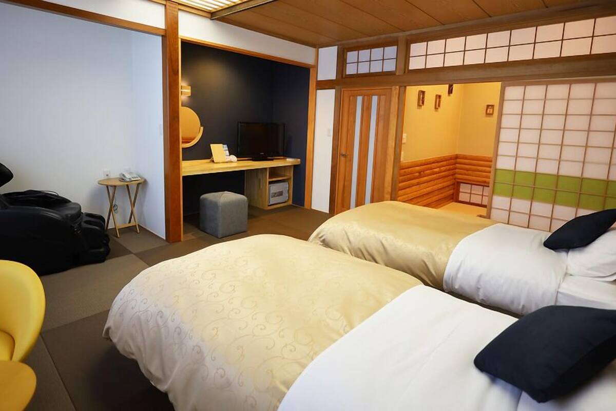 A hotel room with two beds, a desk, a chair, and a TV.