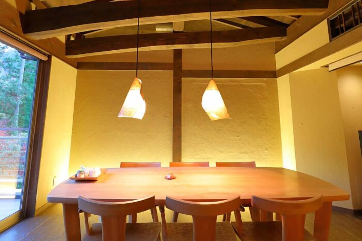 A dining area with a wooden table and chairs, a sloped ceiling with exposed beams, and pendant lighting.