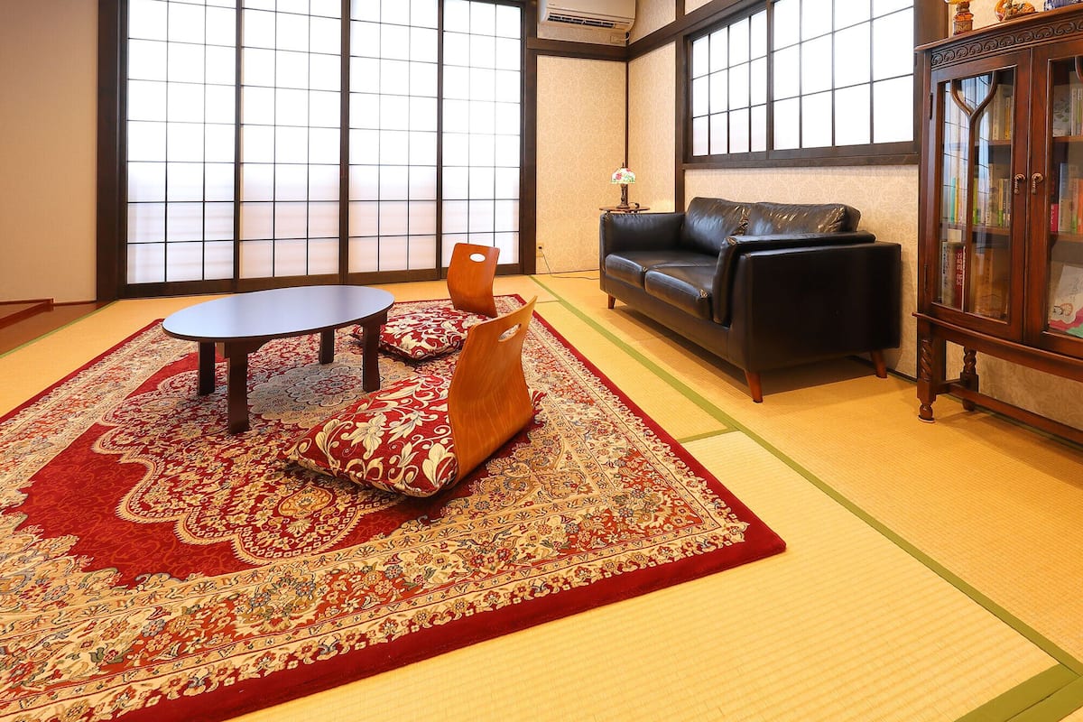 A traditional Japanese room with tatami flooring, a low table, a sofa, and a cabinet with glass doors.