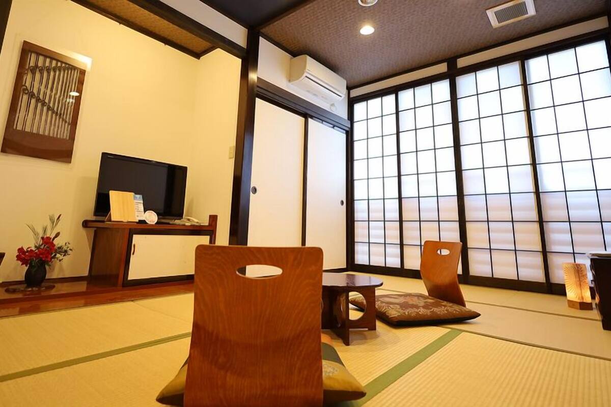 A traditional Japanese room with tatami flooring, a television, a desk, and sliding doors.