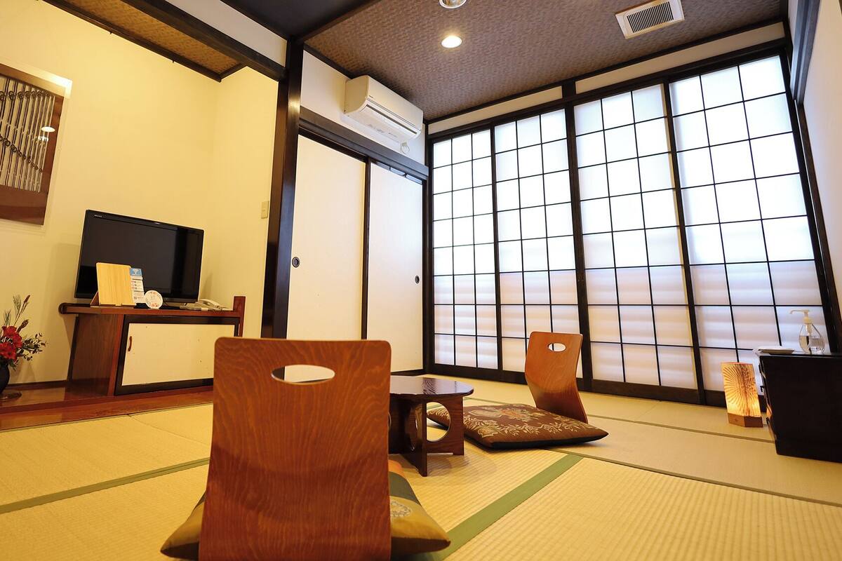 A traditional Japanese room with tatami flooring, a television, a desk, and sliding doors.