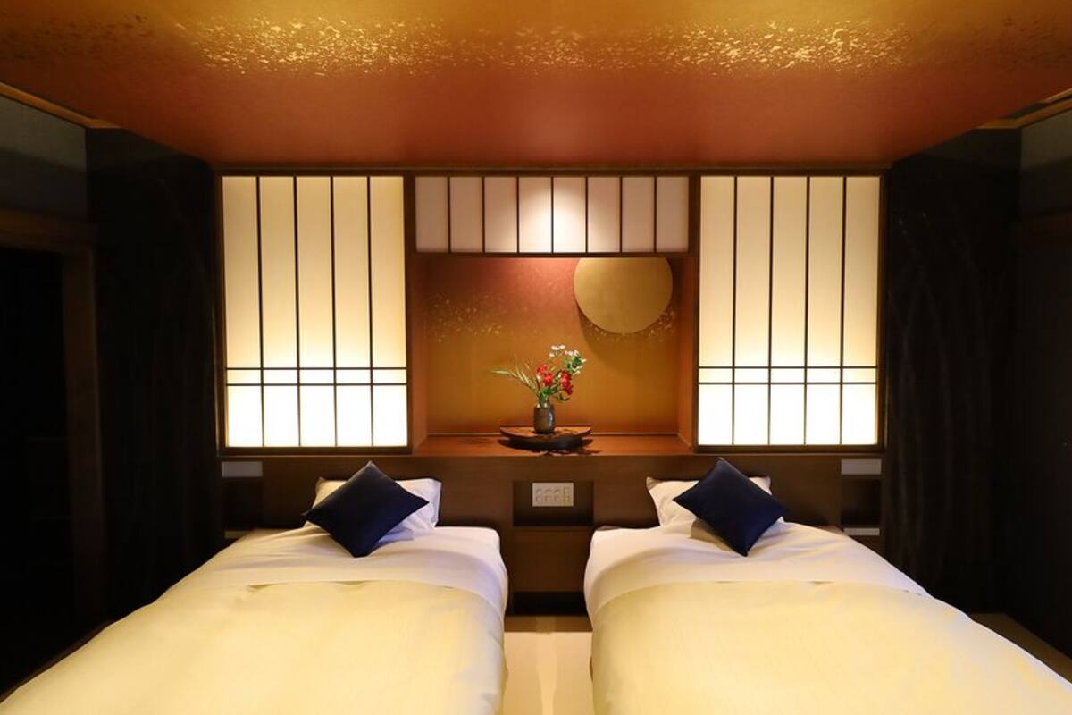 A hotel room with two beds, a decorative wall with vertical panels, a round mirror, and a vase with flowers.