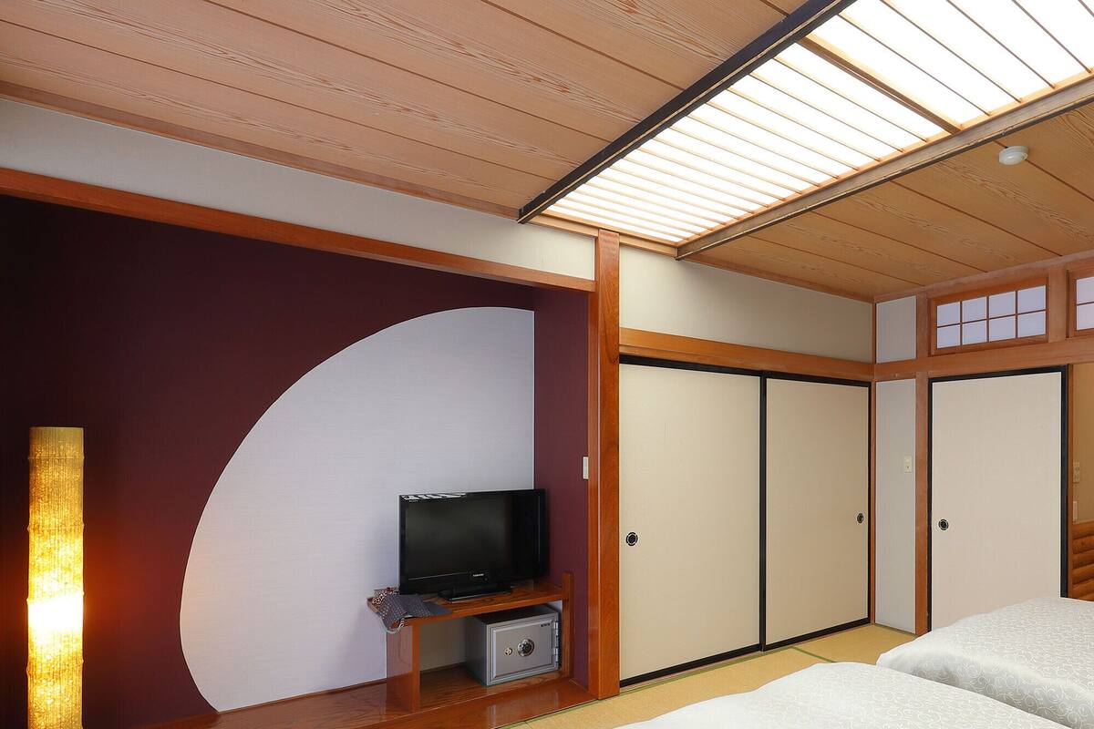A traditional Japanese-style room with tatami flooring, a television on a low wooden stand, and sliding doors.
