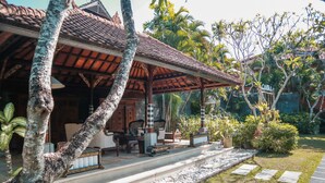 A traditional building with a tiled roof, a covered porch, and a garden with palm trees and potted plants. - The Cakra Hotel (Denpasar)