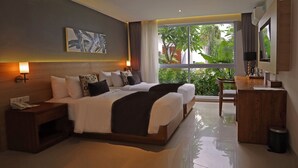 A hotel room with a large bed, bedside lamps, a desk, and a view of greenery outside. - The Cakra Hotel (Denpasar)