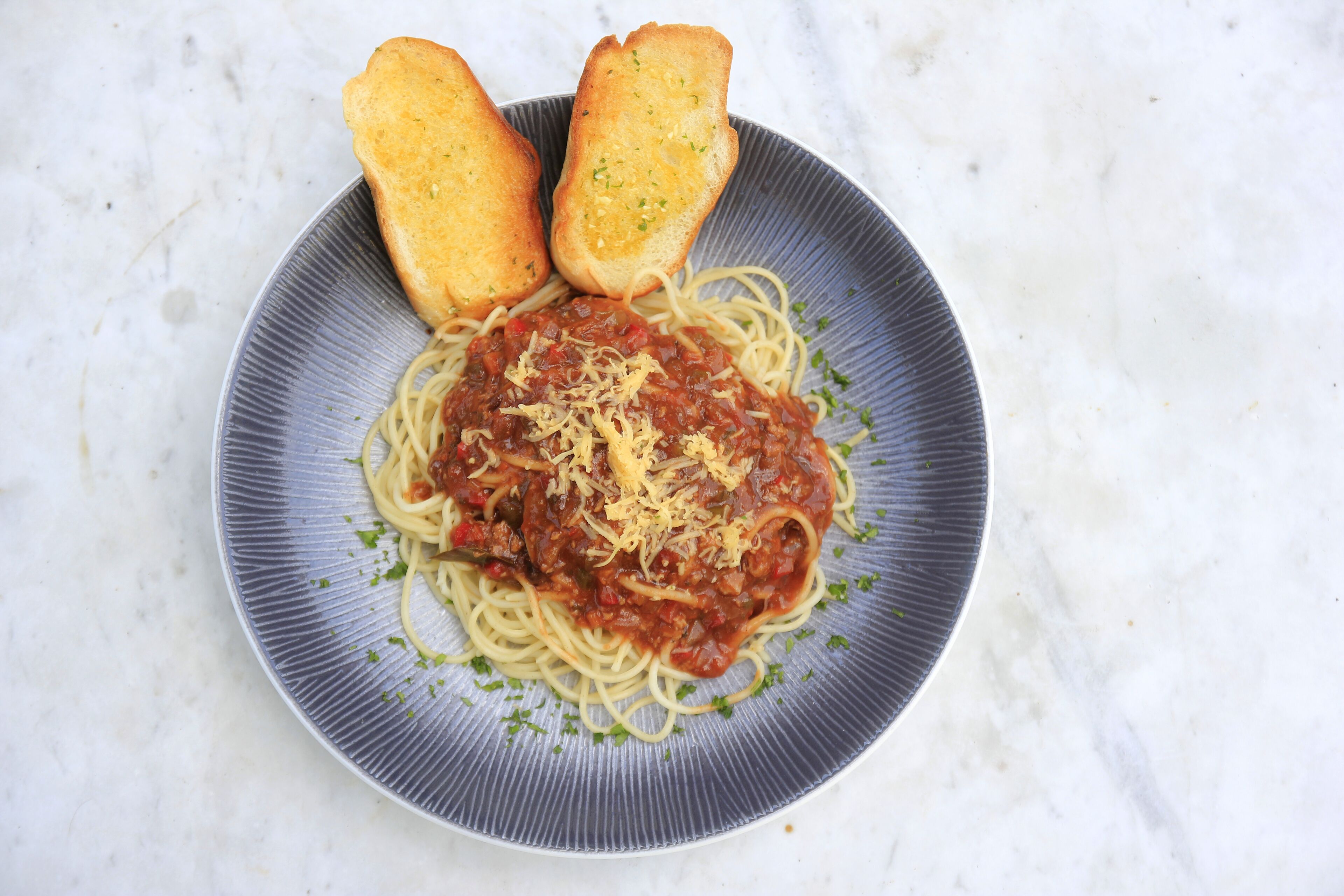 A plate of spaghetti with tomato sauce and grated cheese, accompanied by two slices of toasted bread on a marble surface.