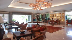 A spacious lobby with wicker furniture, a central coffee table, and a reception desk with a display of items. - The Cakra Hotel (Denpasar)