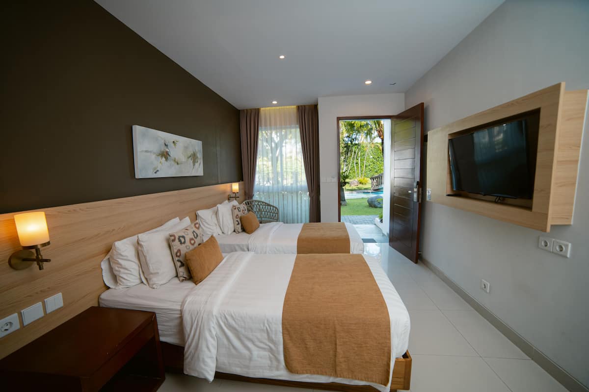Habitación de hotel con dos camas, un televisor en la pared y vista al jardín por la ventana.