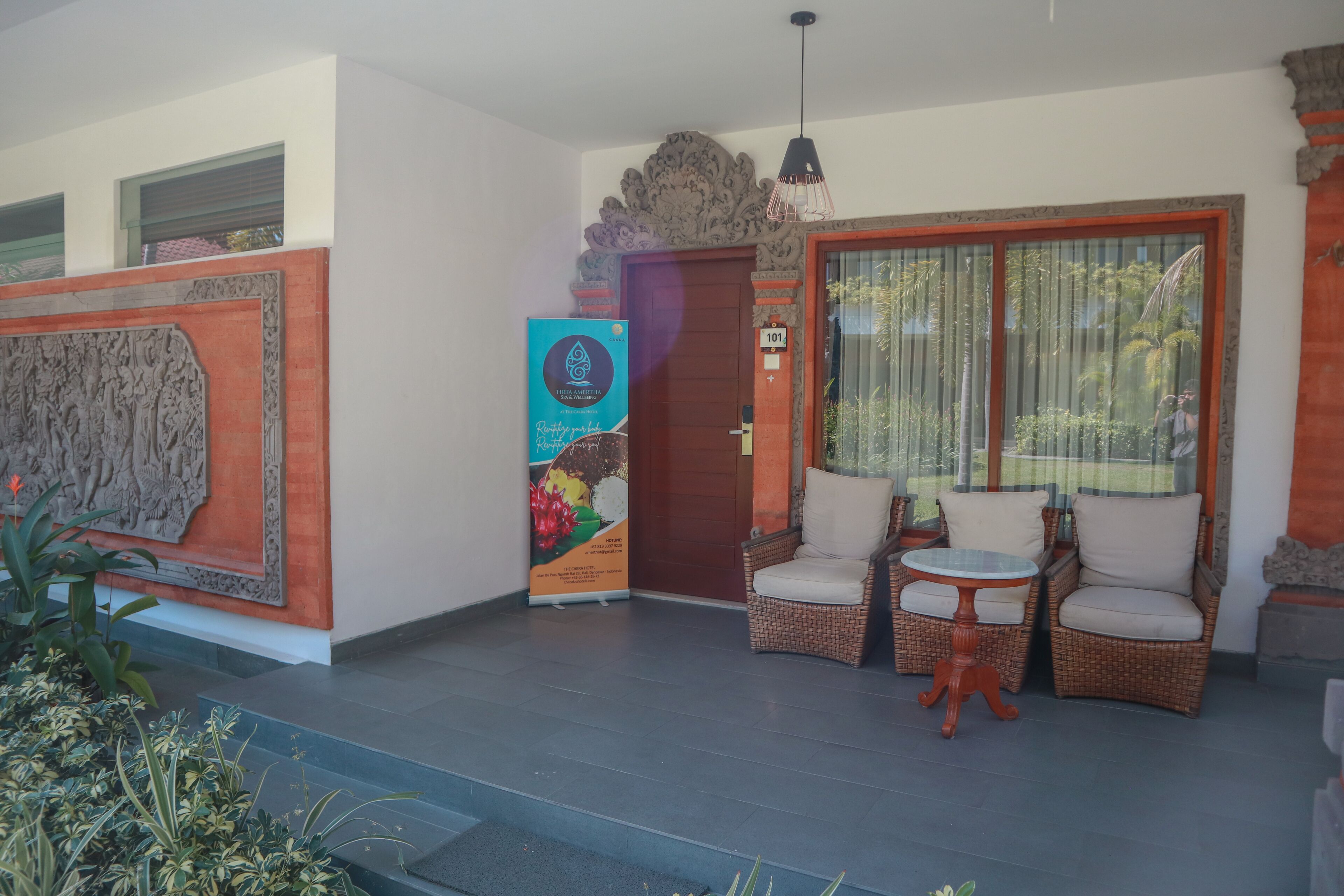 Una zona de recepción con puerta de madera, mobiliario de mimbre y un panel decorativo grande.