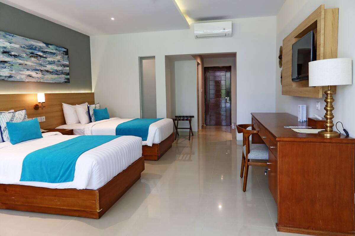 Una habitación de hotel con dos camas, un escritorio, una silla, un televisor y un cuadro en la pared.