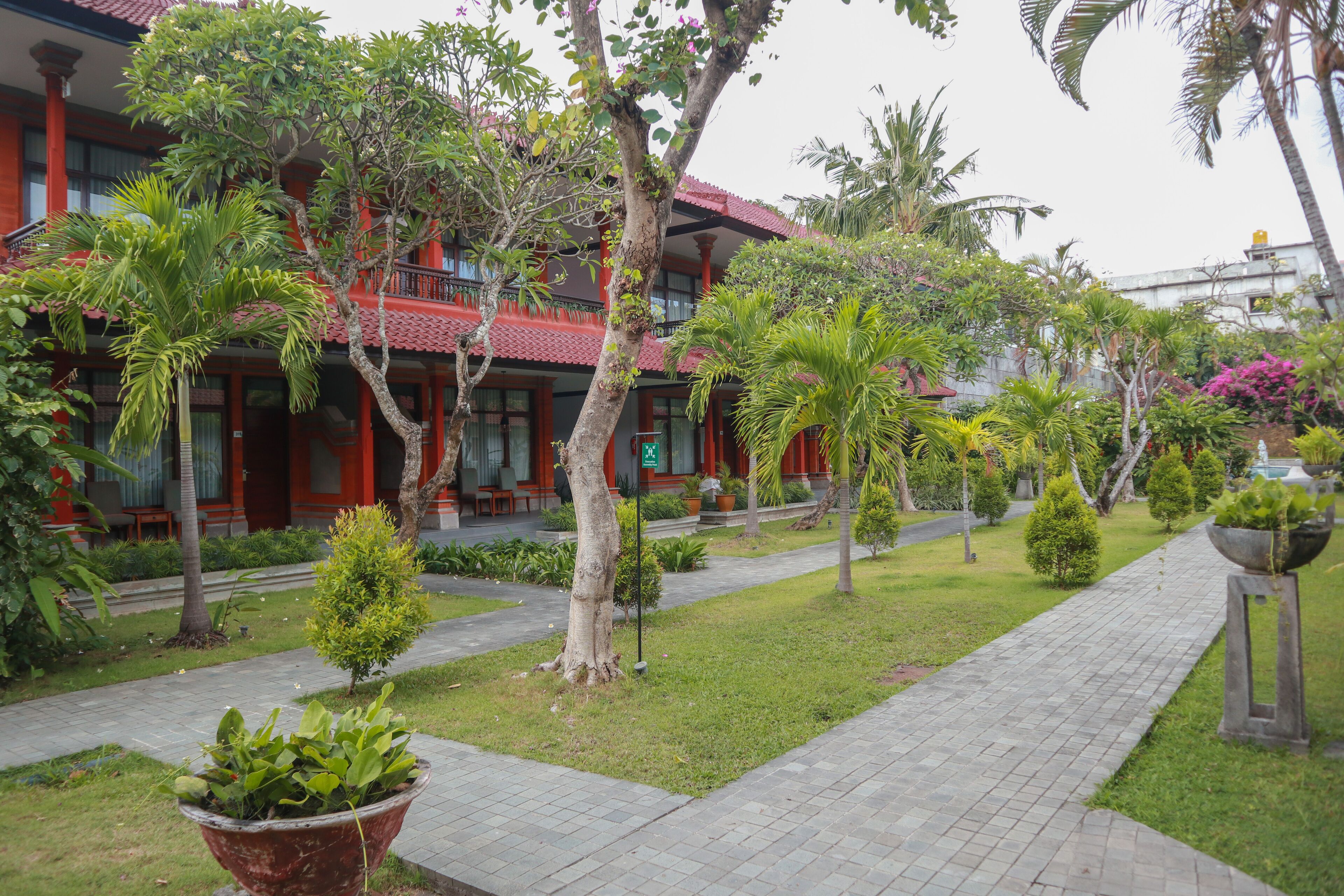 A hotel with a red facade, a paved walkway, and various tropical plants.