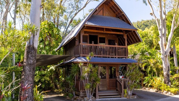 Een houten huis met balkon, omringd door tropische begroeiing.