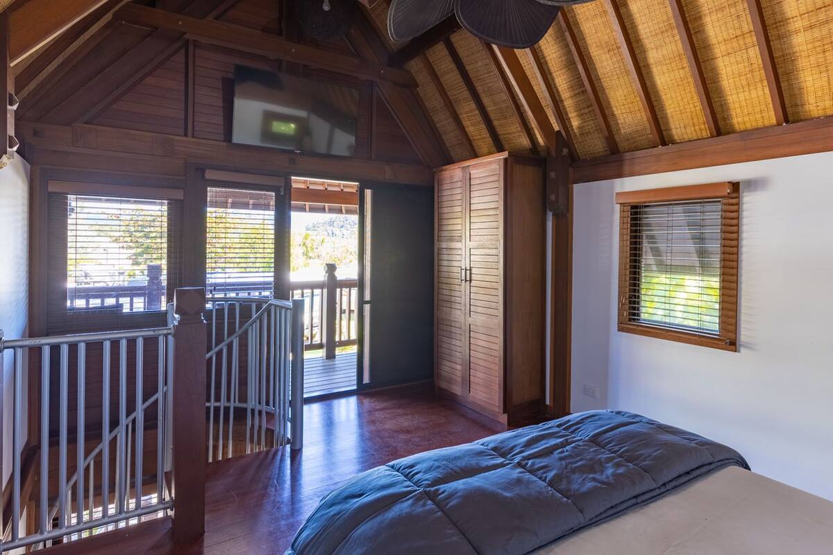 Quarto com cama, ventilador de teto, janela e vista para o exterior.
