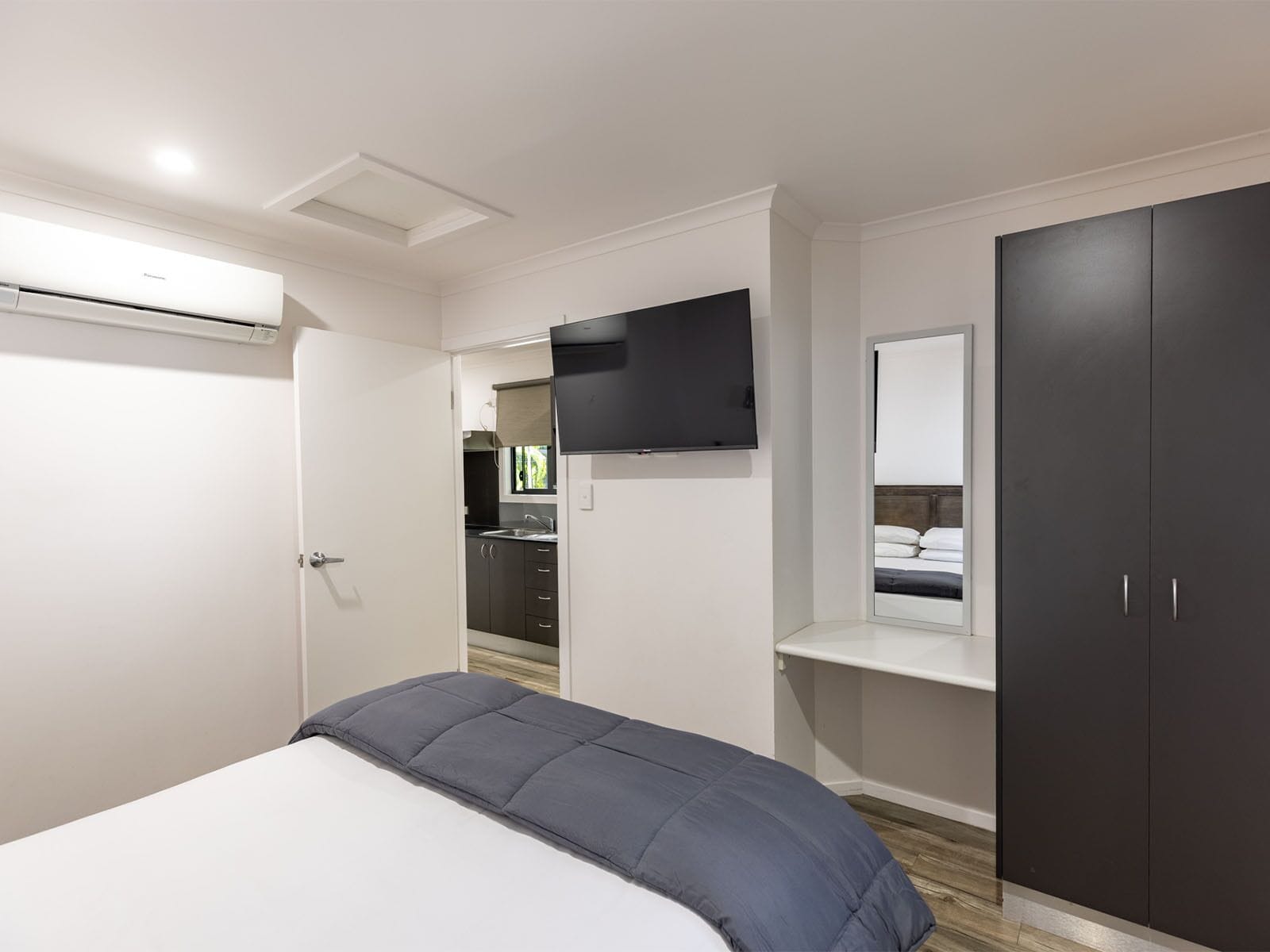 Un dormitorio con una cama, un televisor instalado en la pared, un armario y una pequeña zona de kitchenette.