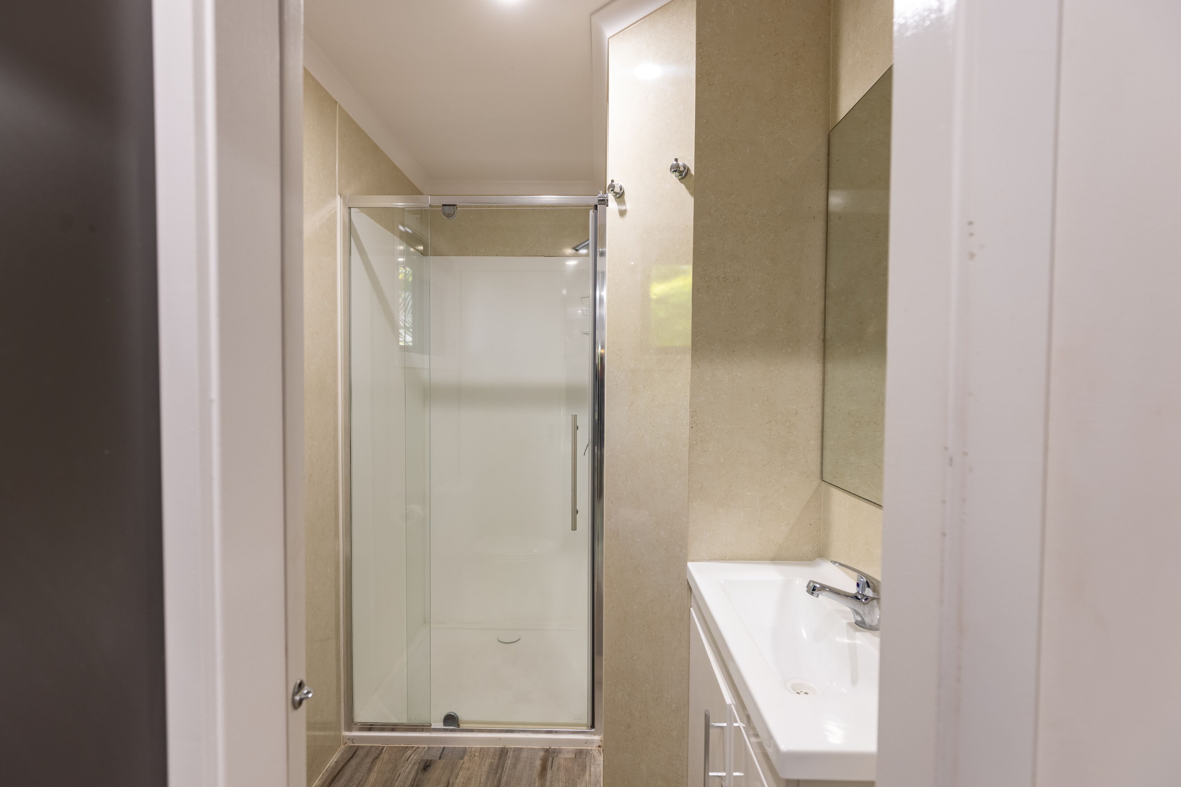 Een moderne badkamer met een douchecabine van glas, een witte wastafel en een grote spiegel.